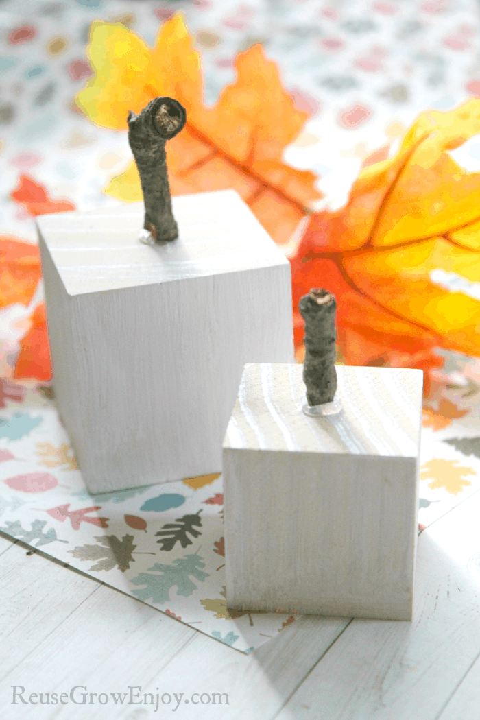 Two wood pumpkins with fall leaves in background