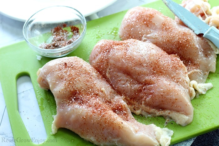 Raw chicken breasts on a green cutting board with a knife to the side. Lightly coated with seasoning mix.