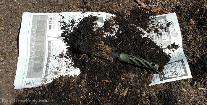 Newspaper being covered with soil in the garden.