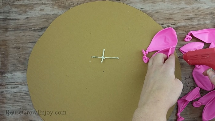 Hand gluing pink balloons to the cardboard with a hot glue gun.