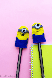 Two minion pencil toppers on pencils with pink background and yellow notebook.