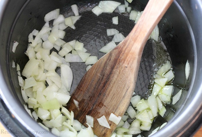 Diced onions being browned in the inner pot of the pressure cooker with a wood spoon.