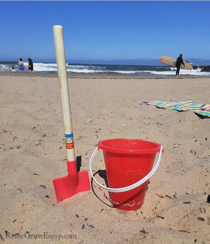 sand bucket on beach with people and surfer in background