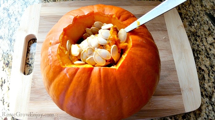 Small pumpkin on a wood cutting board with a spoon scooping out the pumpkin seeds.
